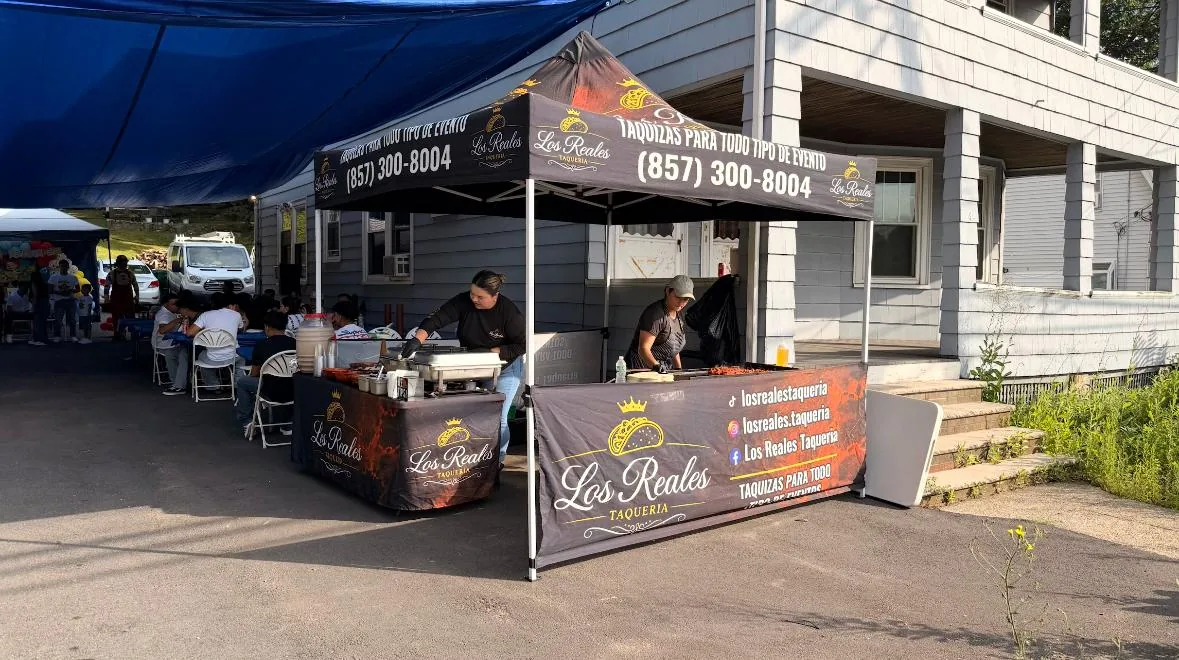 Carpa negra de Los Reales Taquería montada en un evento, con la plancha, los chafers y los invitados sentados al fondo