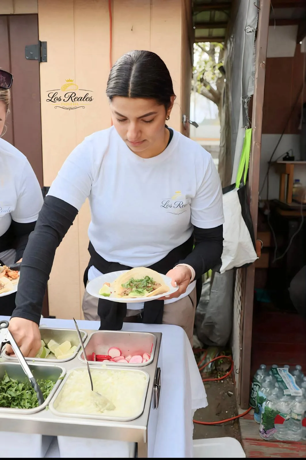 Integrante del equipo de Los Reales Taquería sirve un plato de tacos junto a los complementos de cilantro, cebolla, rábano y limón