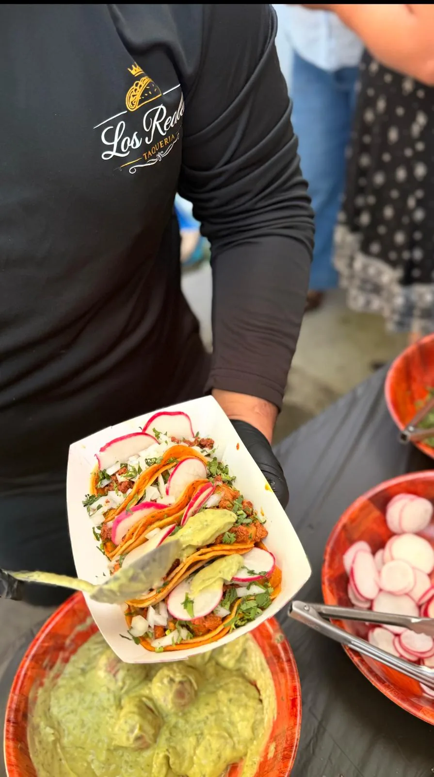 Plato de tacos recién hechos con cilantro, cebolla, rábano y guacamole, servido sobre la barra de complementos