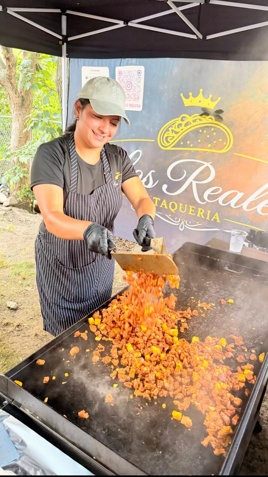 Taquera de Los Reales Taquería voltea carne adobada en la plancha bajo la carpa negra con el logotipo de la corona