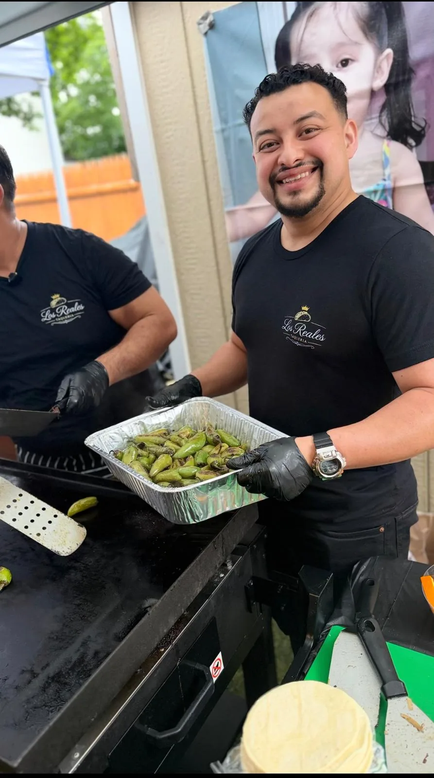 Taquero de Los Reales Taquería con playera de la marca sostiene una charola de jalapeños toreados junto a la plancha